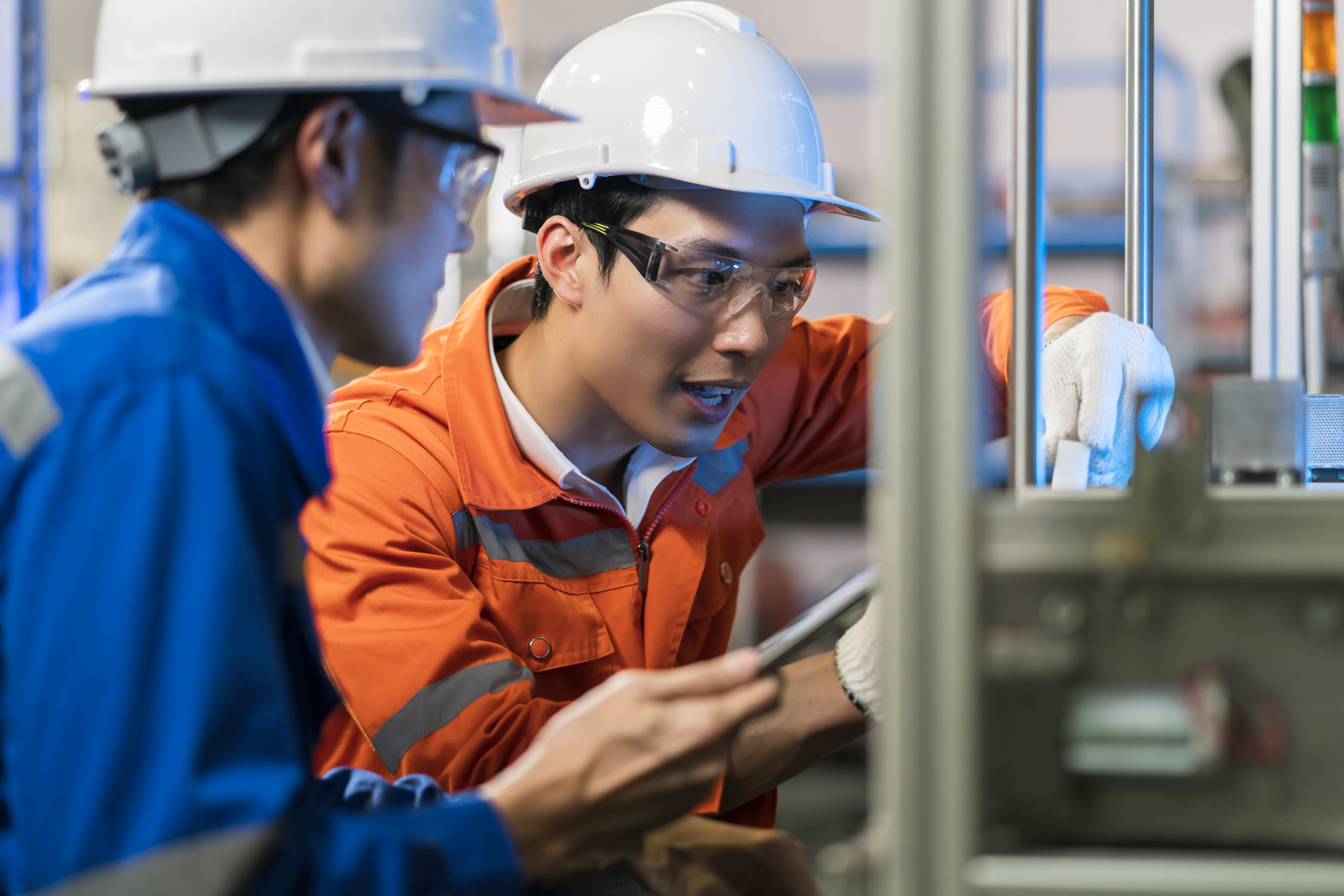 Two engineers wearing safety gear inspect and discuss machinery in an industrial setting. Two engineers wearing safety gear inspect and discuss machinery in an industrial setting.