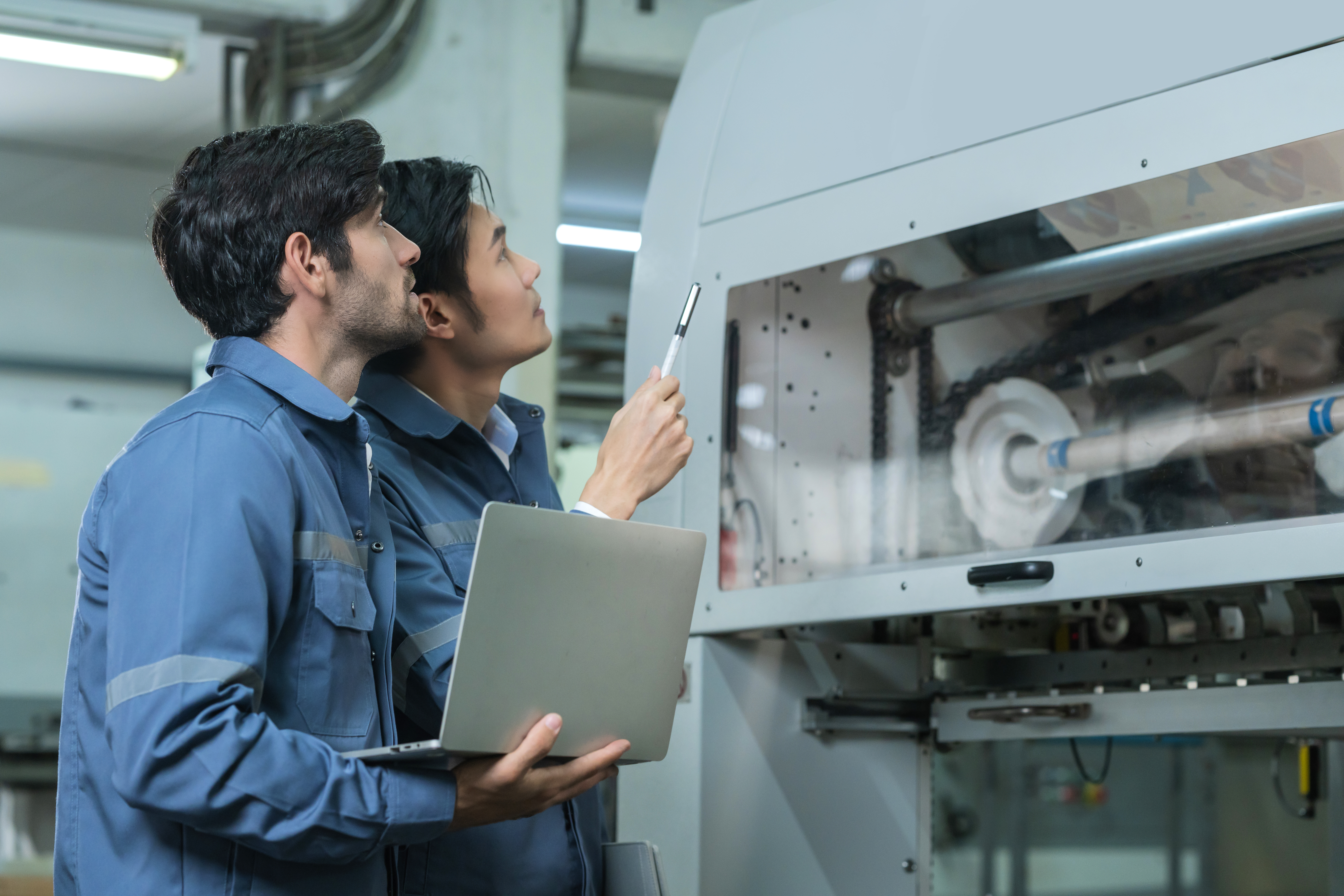 Engineers inspecting machinery with a laptop in a manufacturing facility. Engineers inspecting machinery with a laptop in a manufacturing facility.